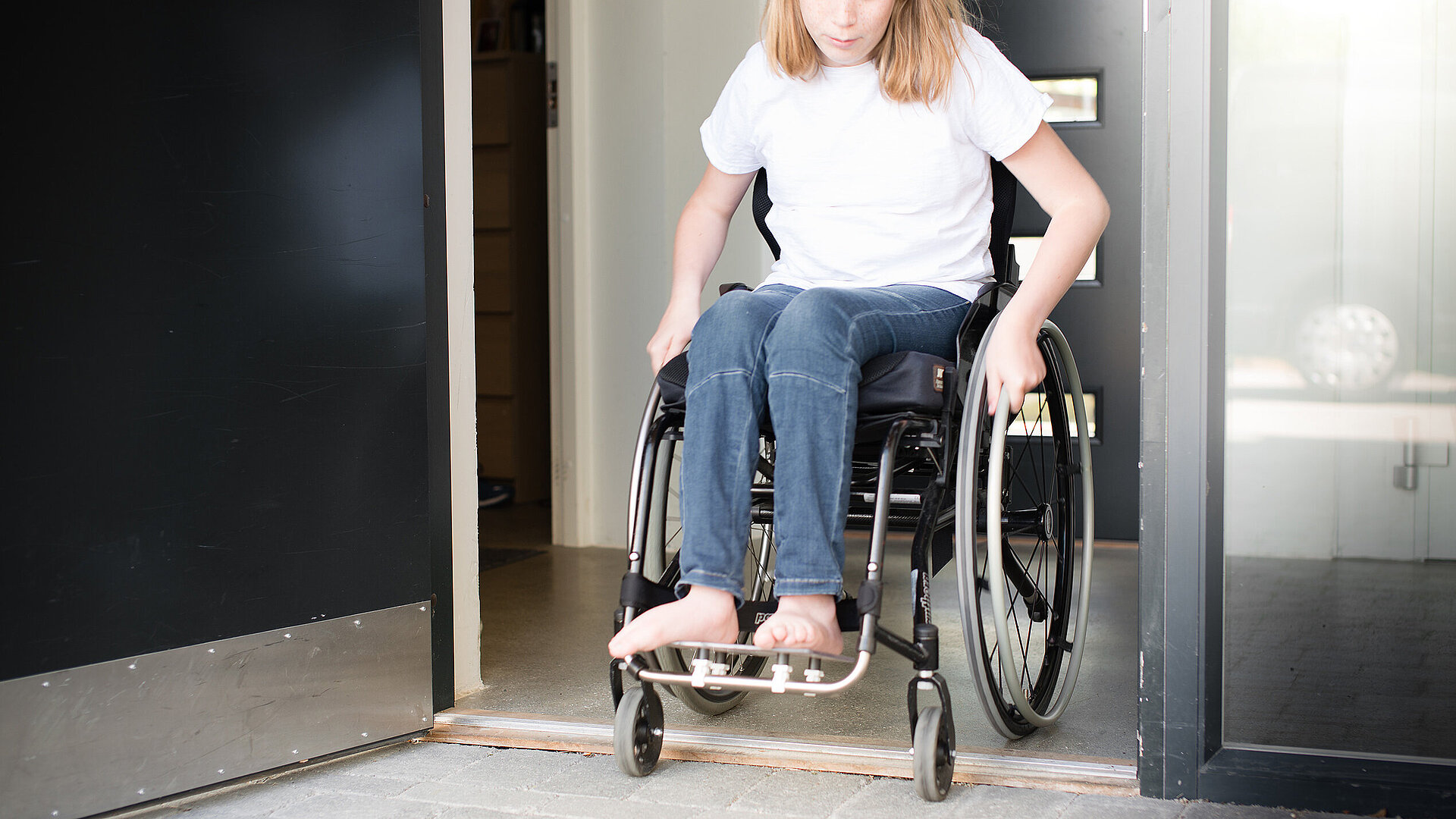 Mädchen in Rollstuhl überrollt niedrige Türschwelle