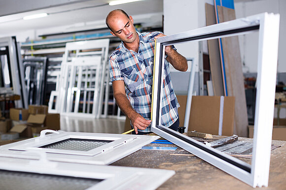 Das Foto zeigt einen Mitarbeiter bei der Kontrolle eines Fensterrahmens innerhalb der Werkseigenen Produktionskontrolle..