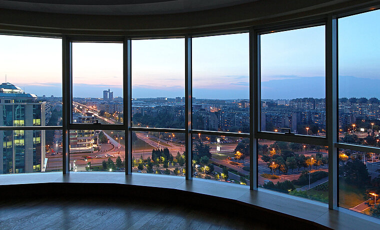 Das Bild zeigt den Blick aus einer breiten Fensterfront auf eine Großstadt bei Nacht.