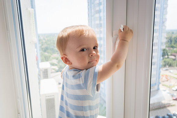 Kleines Kind hält sich am Fenster fest