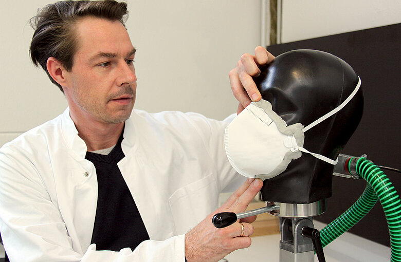 Ein Prüfer in einem Laborkittel prüft eine Atemschutzmaske an einem Prüfkopf