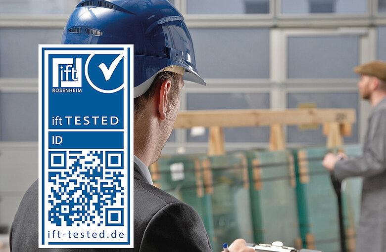 Person with construction helmet notes something on clipboard, in the background another person pushes glass panes through an industrial hall, the ift-tested sign is inserted on the left side of the picture