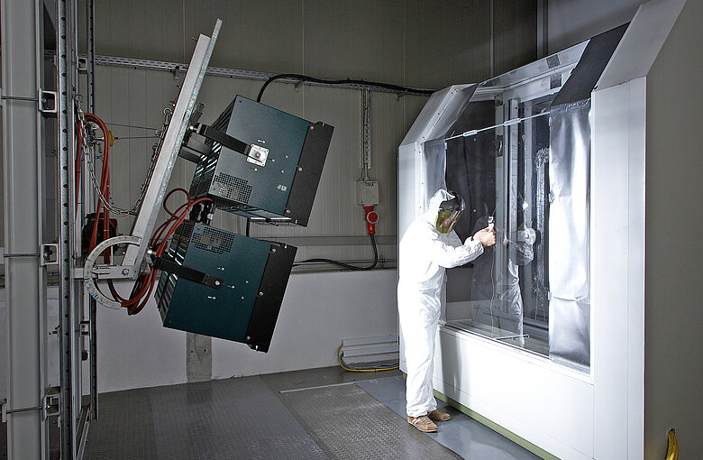 A test engineer in a sun-protective suit stands in front of an illuminated Calimero test rig