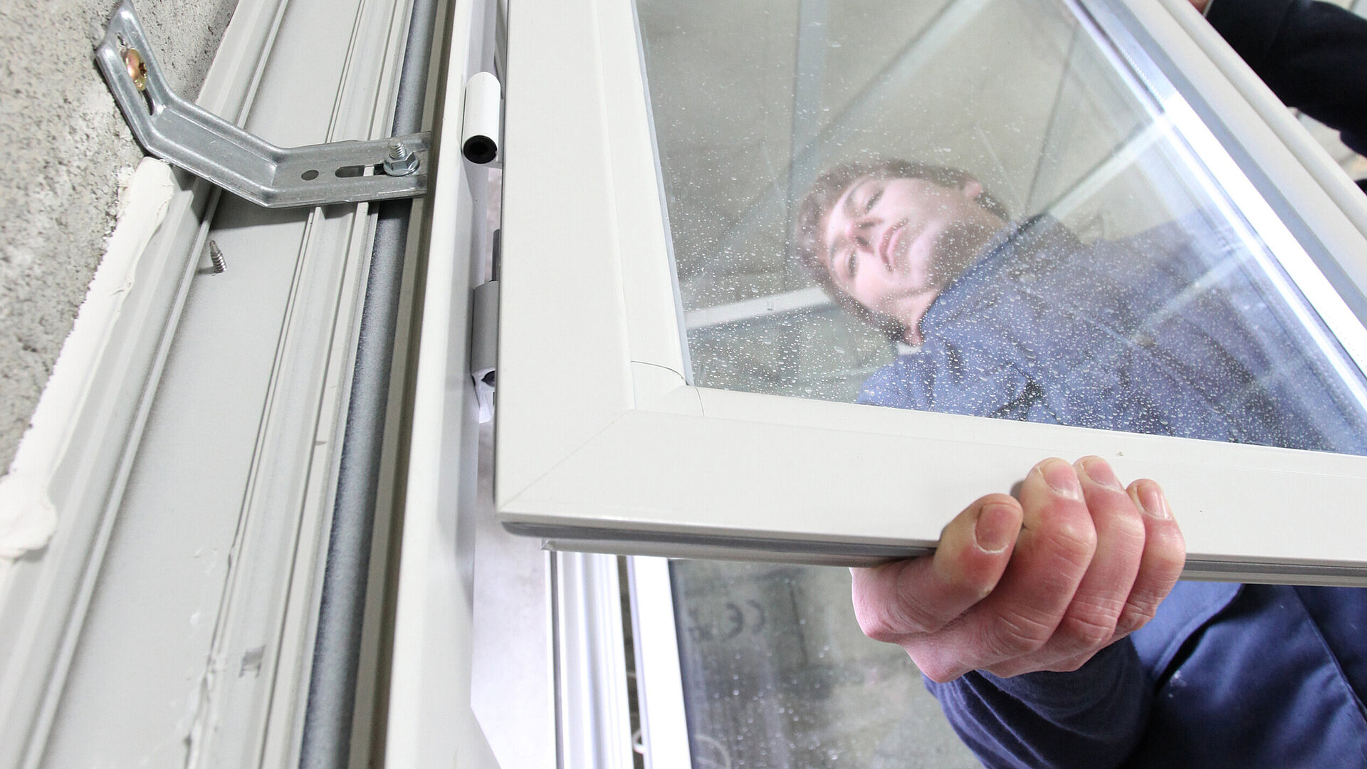 Ein Handwerker montiert vor einer Betonwand einen Flügel an einem Fensterelement. Das Bild steht symbolisch für den Bereich Montage