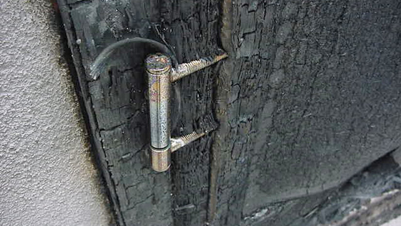 Das Foto zeigt eine Nahaufnahme einer stark verbrannten Holztür nach einer Brandprüfung.
