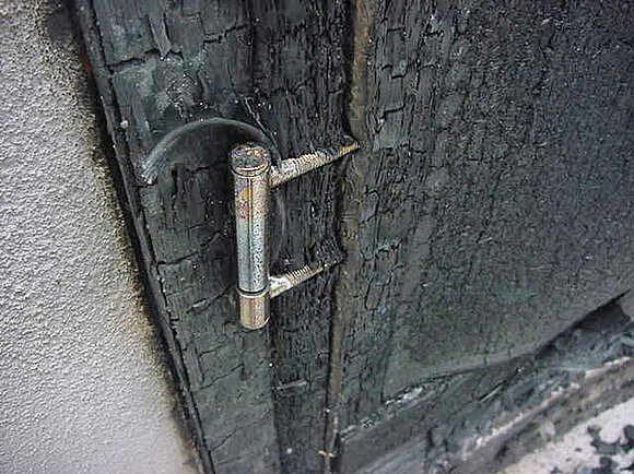 Das Foto zeigt eine Nahaufnahme einer stark verbrannten Holztür nach einer Brandprüfung.