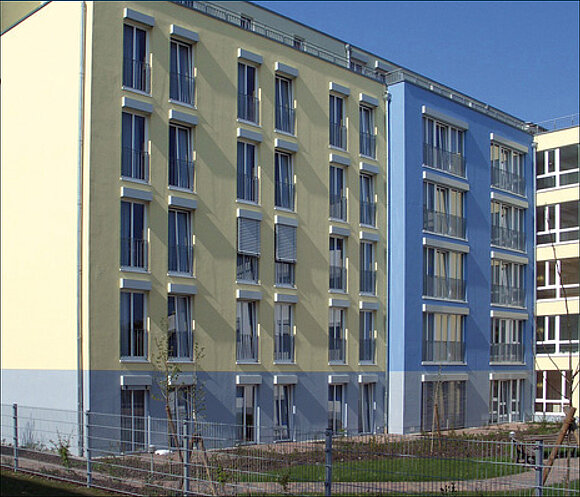 Auf dem Foto sieht man ein Hochhäuserkomplex mit bodentiefen Fensterelementen.
