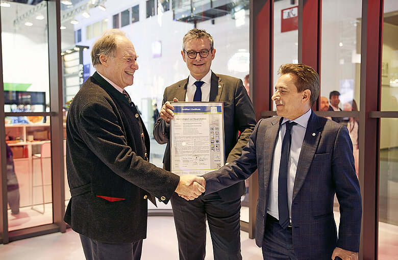 drei Männer bei der Übergabe des Zertifikats für die Nachhaltigkeit von Bauprodukten an Hydro Building Systems Germany GmbH