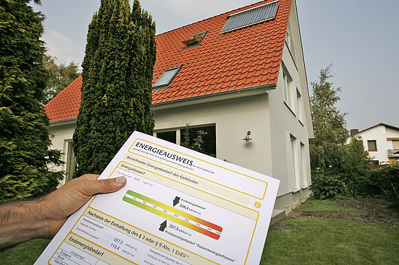 Ein Mann hält vor einem Haus einen Energieausweis in die Luft.