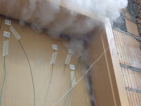 Das Foto zeigt eine Detailaufnahme einer Brandprüfung mit entweichenden Rauchfahnen.