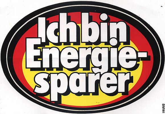 Das Bild zeigt einen ovalen Aufkleber mit der Aufschrift "Ich bin Energiesparer". Der Hintergrund ist schwarz, rot und gelb.